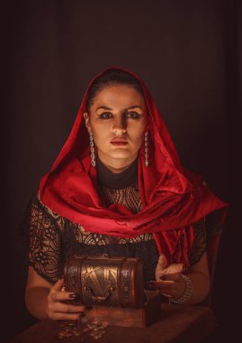 Dişi bir falcı içinde para olan bir kutuyu açar ve keskin bir bakışla bakar. Geleceği tahmin etmek, astral alana ulaşmak.