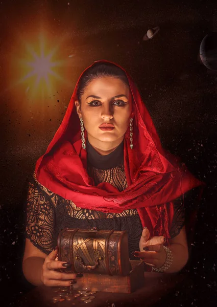 Dişi bir falcı içinde para olan bir kutuyu açar ve keskin bir bakışla bakar. Geleceği tahmin etmek, astral alana ulaşmak.