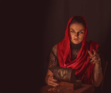 Dişi bir falcı içinde para olan bir kutuyu açar ve keskin bir bakışla bakar. Geleceği tahmin etmek, astral alana ulaşmak.