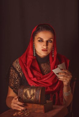 Geleceği tahmin etmek, astral alana ulaşmak. Karanlık bir arka planda elinde kartlar olan falcı delici bakışlarla bakıyor..