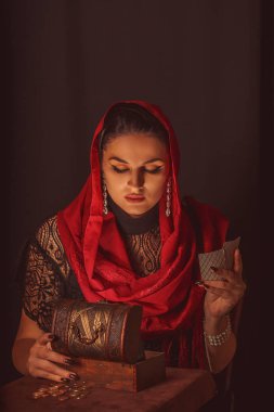 Geleceği tahmin etmek, astral alana ulaşmak. Karanlık bir arka planda elinde kartlar olan falcı delici bakışlarla bakıyor..