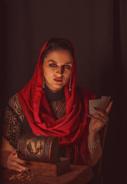Geleceği tahmin etmek, astral alana ulaşmak. Karanlık bir arka planda elinde kartlar olan falcı delici bakışlarla bakıyor..