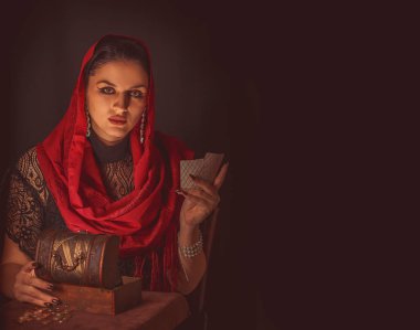 Geleceği tahmin etmek, astral alana ulaşmak. Karanlık bir arka planda elinde kartlar olan falcı delici bakışlarla bakıyor..