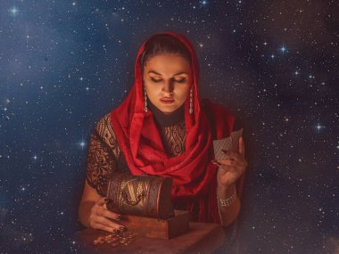 Geleceği tahmin etmek, astral alana ulaşmak. Karanlık bir arka planda elinde kartlar olan falcı delici bakışlarla bakıyor..