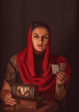 Geleceği tahmin etmek, astral alana ulaşmak. Karanlık bir arka planda elinde kartlar olan falcı delici bakışlarla bakıyor..