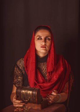 Dişi bir falcı içinde para olan bir kutuyu açar ve keskin bir bakışla bakar. Geleceği tahmin etmek, astral alana ulaşmak.