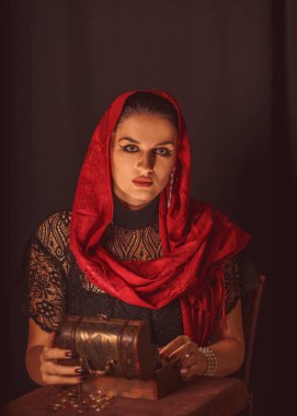 Dişi bir falcı içinde para olan bir kutuyu açar ve keskin bir bakışla bakar. Geleceği tahmin etmek, astral alana ulaşmak.