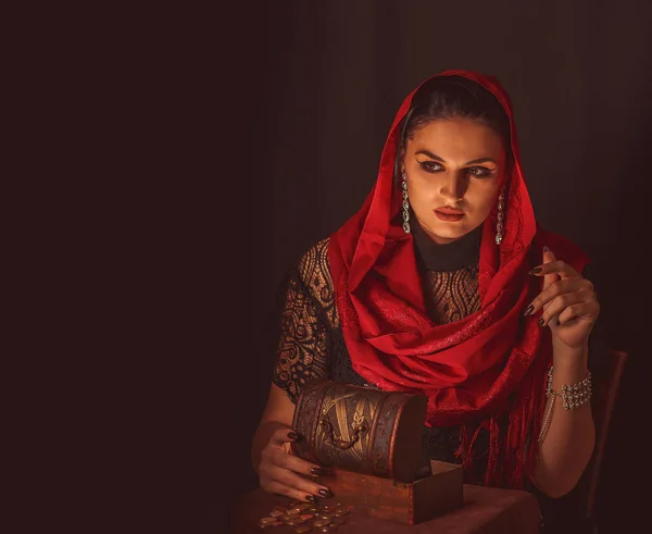 Dişi bir falcı içinde para olan bir kutuyu açar ve keskin bir bakışla bakar. Geleceği tahmin etmek, astral alana ulaşmak.