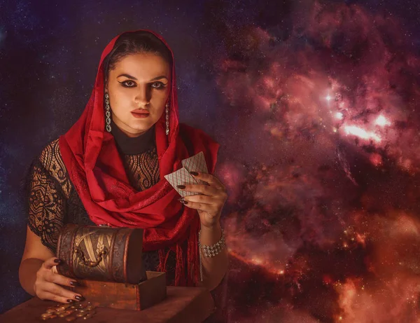 Geleceği tahmin etmek, astral alana ulaşmak. Karanlık bir arka planda elinde kartlar olan falcı delici bakışlarla bakıyor..