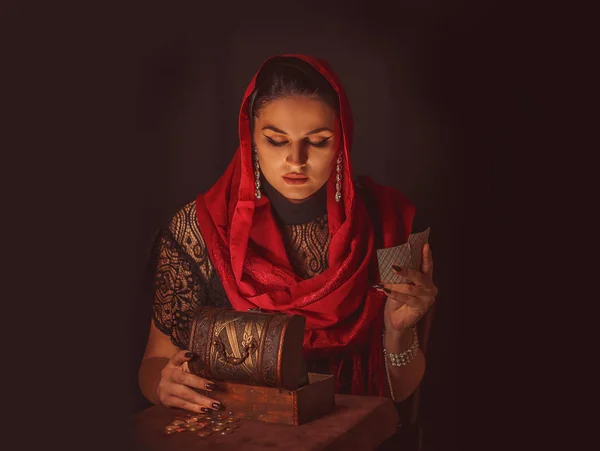 Geleceği tahmin etmek, astral alana ulaşmak. Karanlık bir arka planda elinde kartlar olan falcı delici bakışlarla bakıyor..