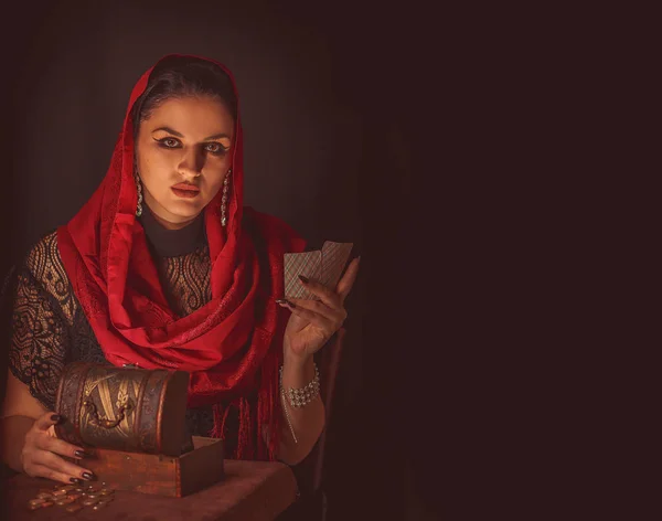 Geleceği tahmin etmek, astral alana ulaşmak. Karanlık bir arka planda elinde kartlar olan falcı delici bakışlarla bakıyor..