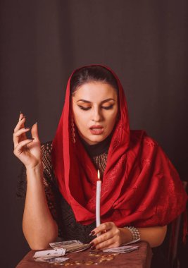 Kafasında eşarp olan ve elinde kartlar olan bir kadın mum ve sikkelerin üzerinde ilahi ilahiler okuyor.