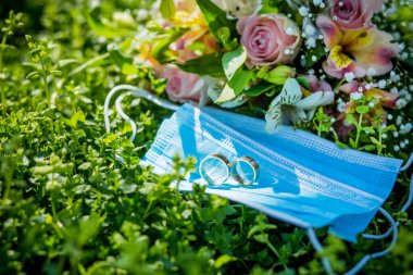 Bir düğün buketinin arka planındaki tıbbi maskelerde iki alyans var. Karantina Düğünü, Coronovirüs