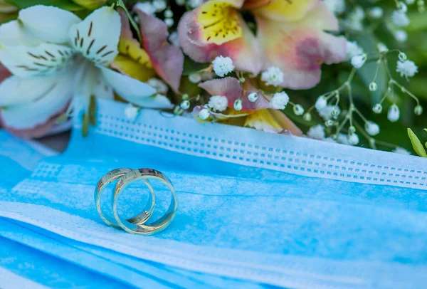 Two wedding rings lie on medical masks on the background of a wedding bouquet. Quarantine Wedding, Coronovirus