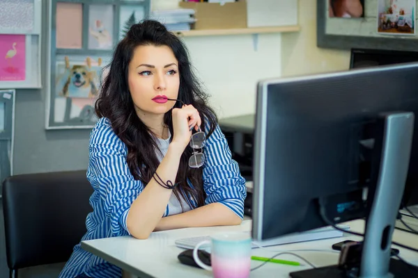 Masada bilgisayar ekranının önünde oturan güzel yaratıcı kız. Tasarımcı bir projeyi yansıtır ve düşünür