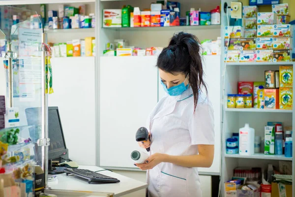 Eczacı içinde ilaç olan bir konteynırı tutuyor ve üzerinde çalışıyor. Yüzünde tıbbi maske olan bir eczacı bilgisayarı yumrukluyor..