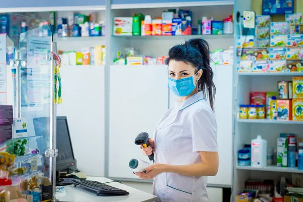 the pharmacist is holding a container with medicine and is studying it. A pharmacist in a medical mask on his face punches medicine in a computer.