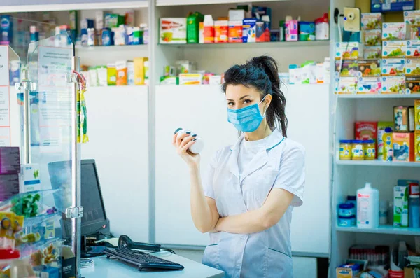the pharmacist is holding a container with medicine and is studying it. A pharmacist in a medical mask on his face punches medicine in a computer.