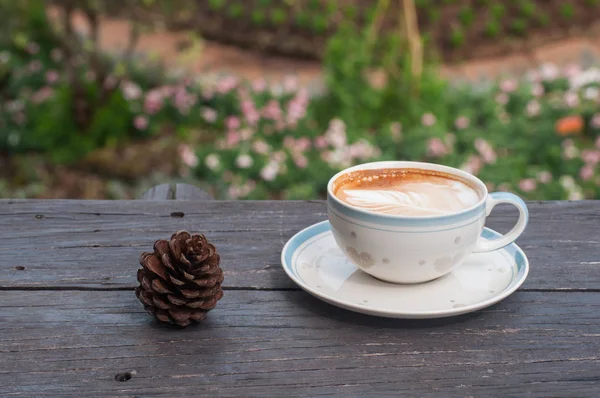 Tasse Kaffee mit Tannenzapfen auf Holztisch im Blumengarten — Stockfoto