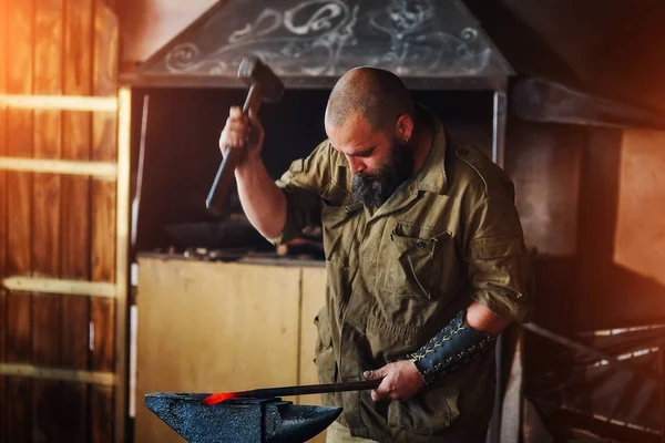 Herrero trabajando en la fragua. Fabricación de piezas y armas de metal fundido, utilizando el martillo y el yunque . — Foto de Stock