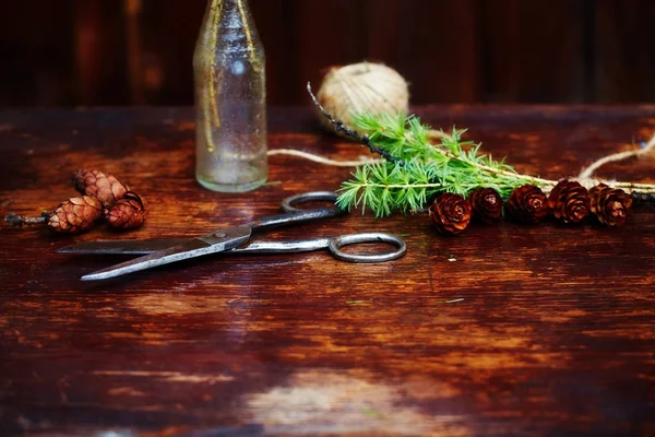 Arrière-plan en bois de Noël.Branches et cônes en épicéa dans une bouteille vintage, les vieux ciseaux et le cordon rusé. Le concept des ensembles d'entraînement pour Noël . — Photo