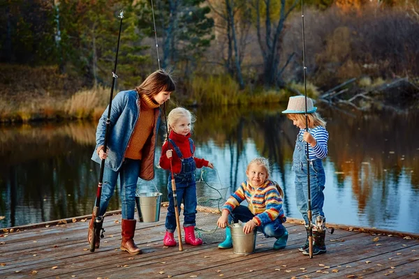 Quattro bambine pescano pesci su un pontone di legno. Weekend al lago. Pesca con gli amici . — Foto Stock