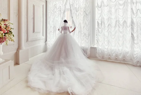Die Braut steht am Fenster in einem Kleid mit langer Schleppe — Stockfoto