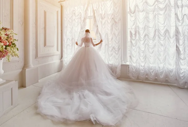 Schöne Braut mit langer Schleppe, die am Fenster steht. — Stockfoto