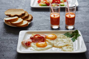 Her gün kahvaltı. Sahanda yumurta ile pastırma, havuç suyu, sebze salatası, ekmek. Karanlık taş arka plan üzerinde
