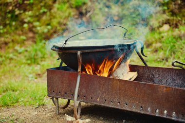 Açık hava pişirme alanı. Kazan kaynıyor, yemek ateşte ve yakacak odununda pişiriliyor.