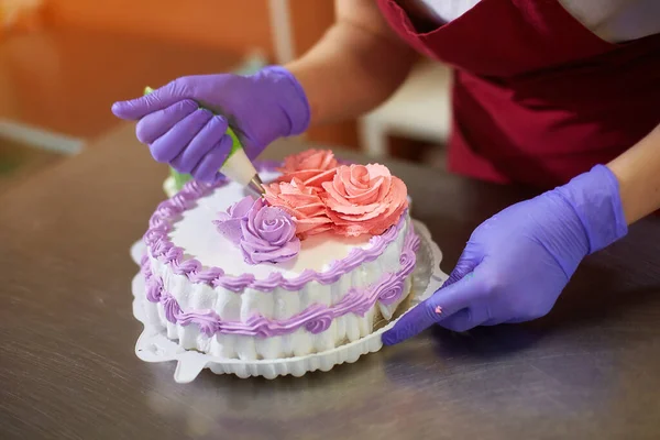 Pastry chef decorates the cake with flowers from the cream.  The cream is squeezed out of the pastry bag through a special nozzle.