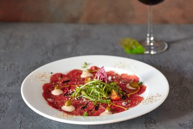 Ahşap zemin üzerinde beyaz bir tabakta et carpaccio, lezzetli bir ekmek ve bir bardak şarap ile