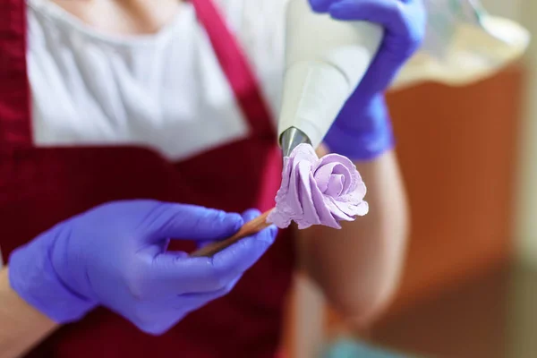 The pastry chef makes a rose flower out of buttercream to decorate the cake. The cream is squeezed out of the pastry bag through a special nozzle