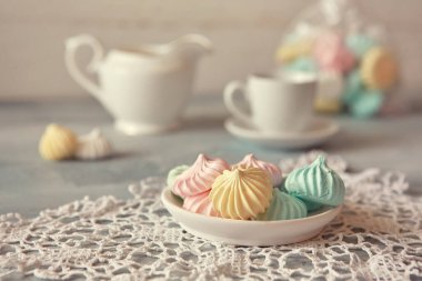 Pastel gölgeli çok renkli kremalar ve açık ahşap bir arka planda bir sürahi. Kahvaltının yanında çay ya da kahve konsepti, ev konforu ve şefkat. Yakın çekim, seçici odaklanma.