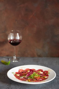 Ahşap zemin üzerinde beyaz bir tabakta et carpaccio, lezzetli bir ekmek ve bir bardak şarap ile.