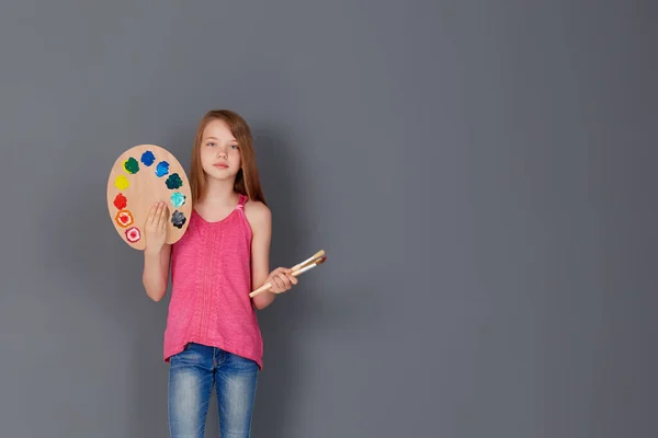 グレーの壁にパレットとブラシを持つ女の子 子供の創造性の概念 テキストのスペース — ストック写真