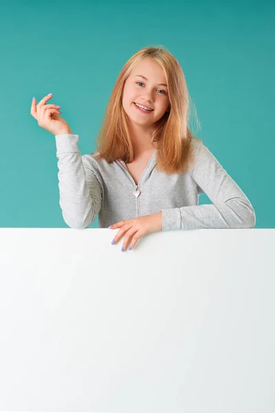 Retrato de una hermosa joven sobre un fondo turquesa, de pie detrás de una pancarta blanca para su texto —  Fotos de Stock