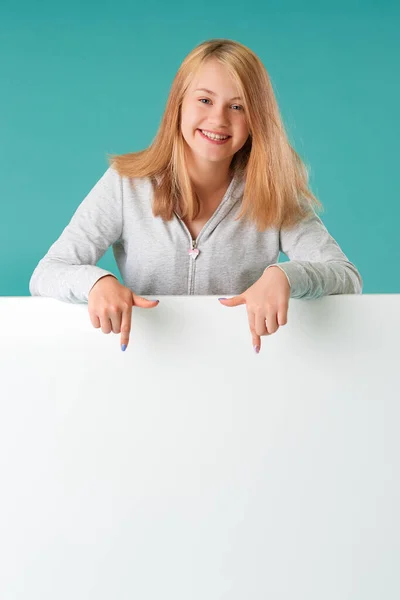 Retrato de uma menina bonita em um fundo turquesa, de pé atrás de uma bandeira branca para o seu texto — Fotografia de Stock