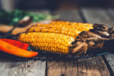 Koyu ahşap bir arka plan üzerinde ahşap bir tahta üzerinde otlar ile koçan üzerinde ızgara mısır.