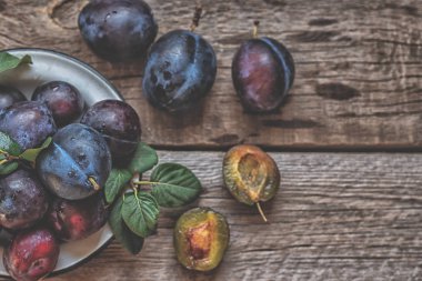 Yeşil yapraklı rustik masada eski bir kapta taze erik yığını. Tonlu görüntü. Yumuşak odak. Kopyalama alanı.
