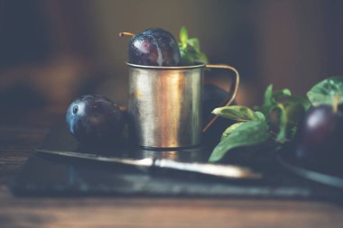 Rustik arka planda erikler. Mavi erik meyvesinin yarısı ve tamamı. Yaprakları ile birçok güzel erik. Taze organik meyveler. Yemek geçmişi. Sağlıklı yiyecekler. Tonlu görüntü.