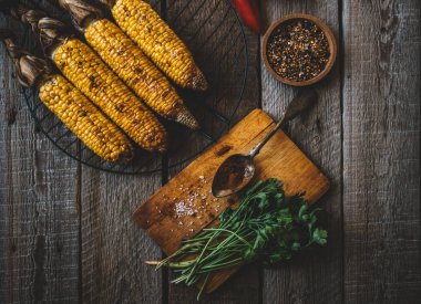 Mutfak masasının en üst manzarasında, ahşap masada erimiş tereyağı ve sebze ile ızgara mısır koçanı. Organik sarı mısır yenmeye hazır. Kopyalama alanı olan düz.
