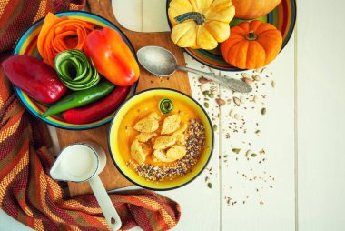 Sıcak sonbahar balkabağı çorbasıyla ahşap kırsal masa manzaralı, kasede susam tohumları süslenmiş. Cadılar Bayramı menüsü için rahat bir yaşam tarzı.