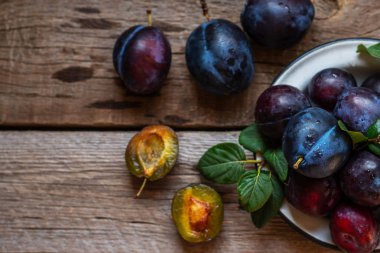 Eski bir ahşap yüzey üzerinde yeşil yapraklı taze mavi erik. Sonbahar hasadı. Sonbahar hasat arka plan. Sağlıklı vejetaryen yemekleri. Biyo, organik yemek. Üst te. Kopyalama alanı.