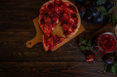 Koyu ahşap tahta arka plan üzerinde Rustik erik pasta. Sonbahar hasadı. Pasta ve yapraklı taze erik. Sağlıklı, organik gıda. Üst te. Tonlu görüntü.