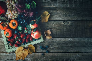 Sağlıklı meyveler. Çilek, böğürtlen, üzüm, hurma ve kır ağacından arkaplanda nar dolu eski bir tepsi. Tonlanmış görüntü. Seçici odaklanma. Üst Manzara. Boşluğu kopyala.