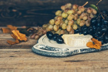 Peynir, koyu mavi ve beyaz üzüm eski ahşap arka plan üzerinde sonbahar yaprakları ile. Sağlıklı meyveler. Şarap üzüm arka plan. Bir demet üzüm yemeye hazır. Tonlu görüntü. Seçici odaklama.