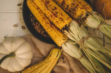 Köhne mutfak masasında ızgara mısır koçanı ve ahşap tahtada yeşillikler. Meksika baharatlı ızgara tatlı mısır. Sağlıklı yaz ya da sonbahar yemekleri.