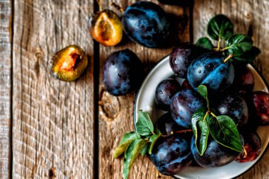 Eski bir ahşap yüzey üzerinde yeşil yapraklı taze mavi erik. Sonbahar hasadı. Sonbahar hasat arka plan. Sağlıklı vejetaryen yemekleri. Biyo, organik yemek. Üst te. Kopyalama alanı.