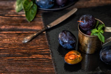 Siyah taştan bir tabakta yaprakları olan erikler. Kırsal gıda geçmişi. Taze organik meyveler. Sağlıklı yiyecekler. Tonlanmış görüntü. Metnin için boş yer. Üst Manzara. Boşluğu kopyala.
